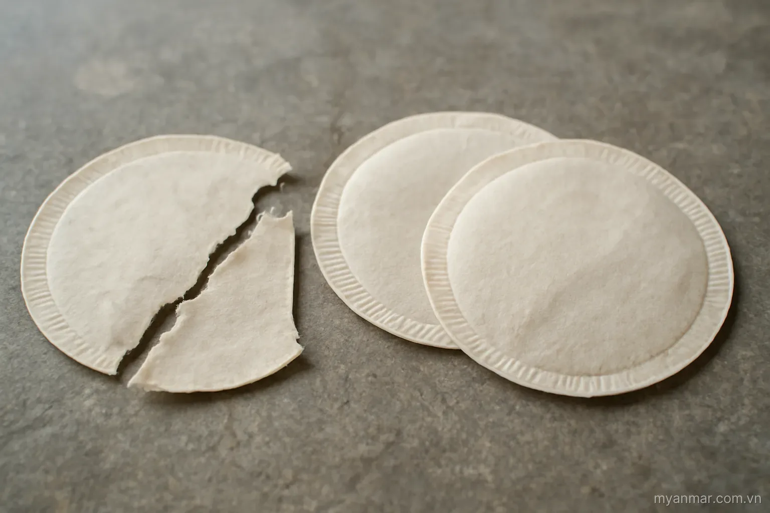 A torn cloth filter beside two intact ones on a stone surface, close view, no text