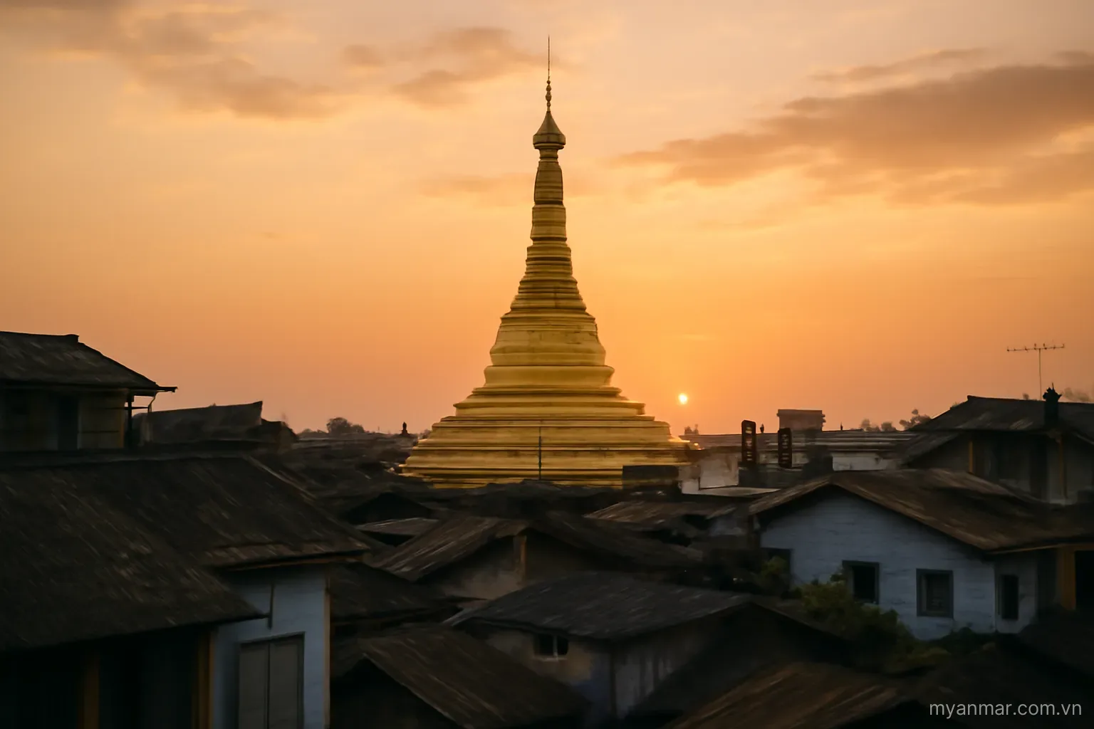 A golden pagoda spire rising above rooftops at sunset, wide view, no text