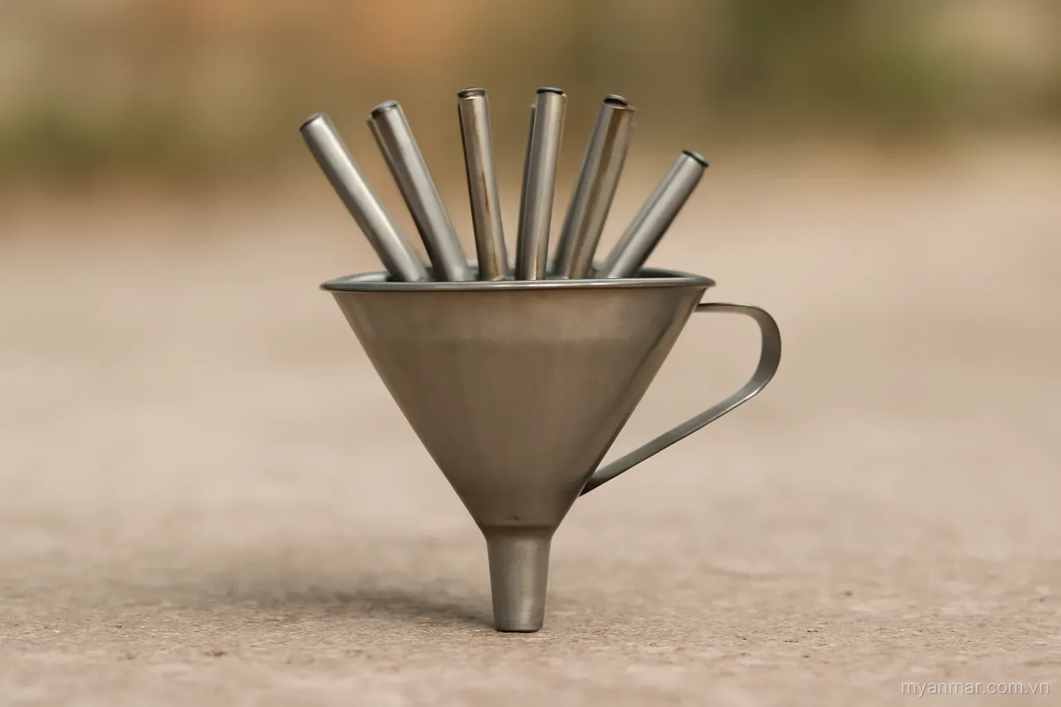 A funnel with several narrow spouts feeding into its wide mouth, side view on plain ground, no text