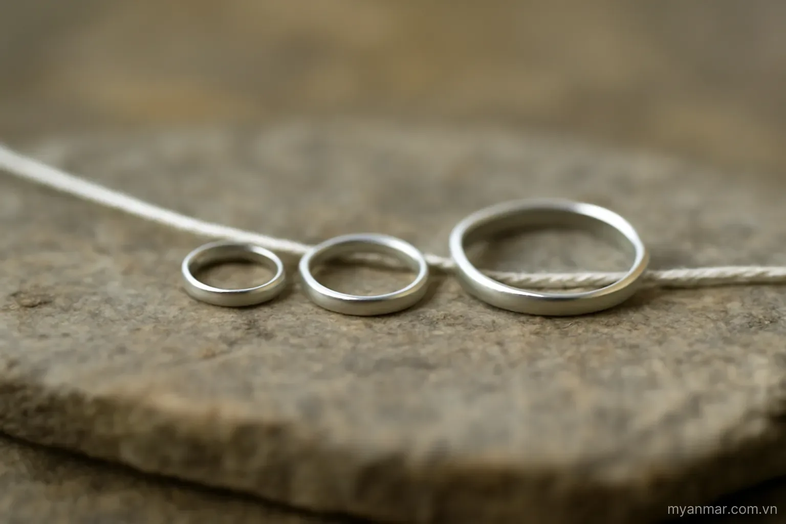 Three small rings of different sizes lined up in a row on a flat stone with a thread through them, no text